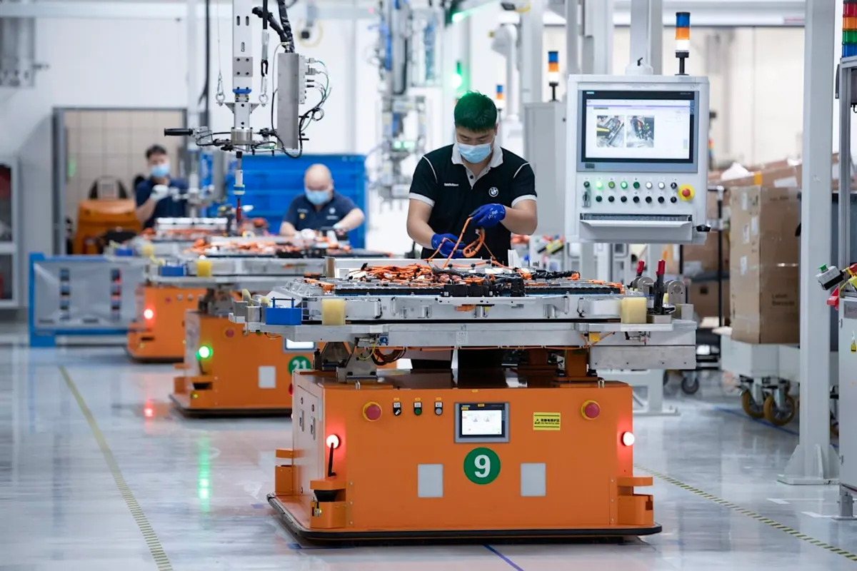 Workers assembling battery wiring on orange automated guided vehicles in a BMW production line