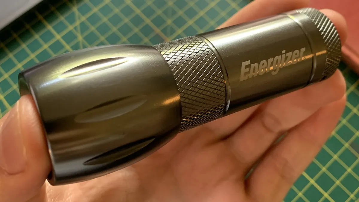 Hand holding the original grey aluminium Energizer compact torch with knurled grip over a cutting mat